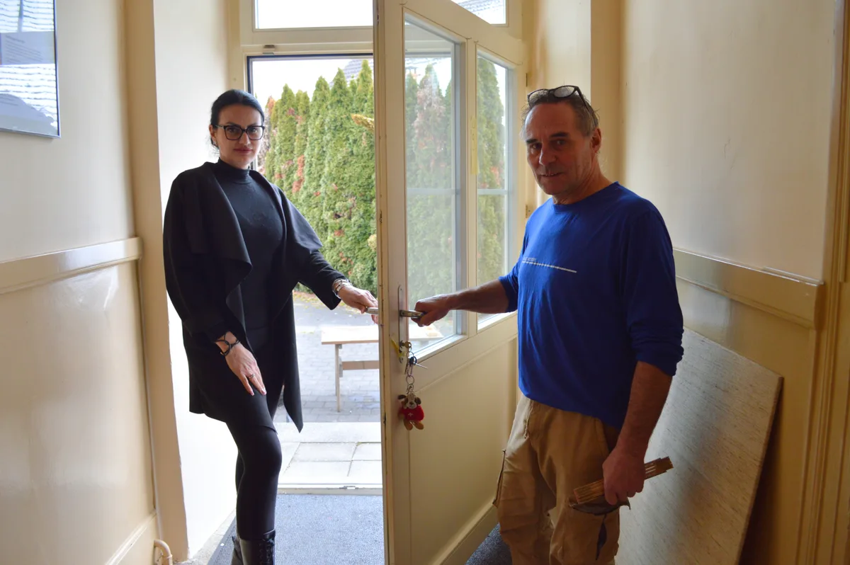 Die Wirtin und ein Handwerker stehen bei einer Tür.